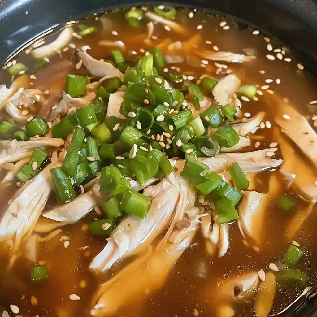 Delicious shredded chicken soup garnished with chopped green onions and sesame seeds, served in a flavorful broth. Perfect for a comforting meal.