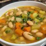 Hearty vegetable bean soup with carrots, celery, and herbs in a white bowl, perfect for a nutritious meal.